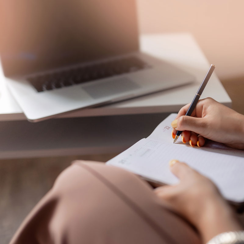 Frau sitzt an einem Laptop und notiert sich etwas im Kalender